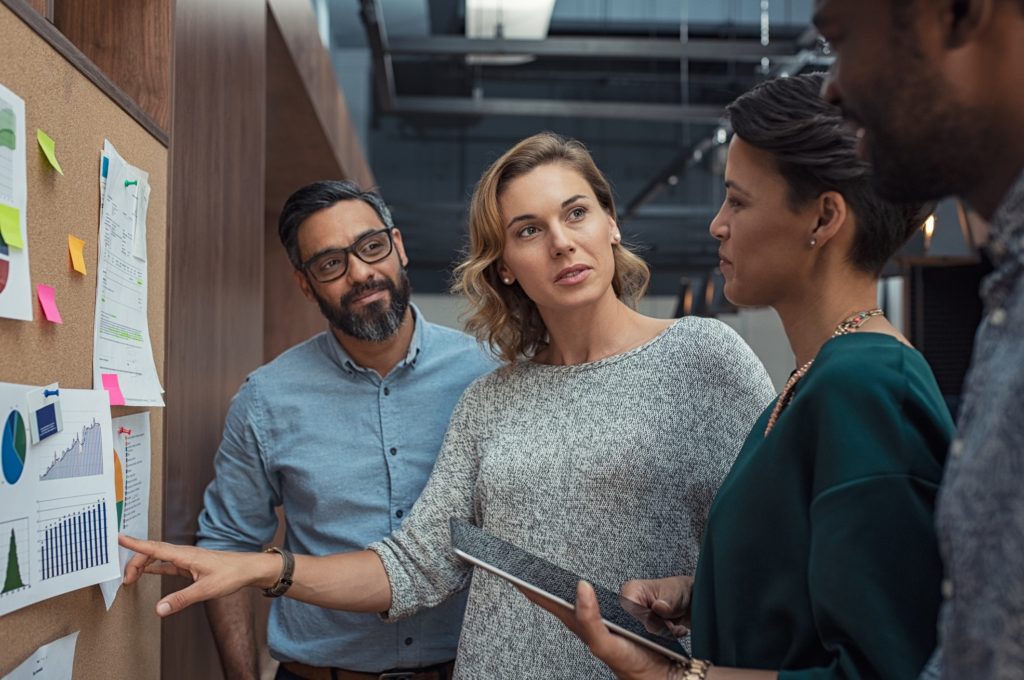 Women discussing a project status, looking at a project management board.