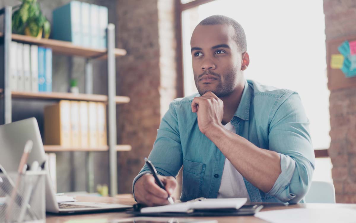 man thinking while writing in notebook