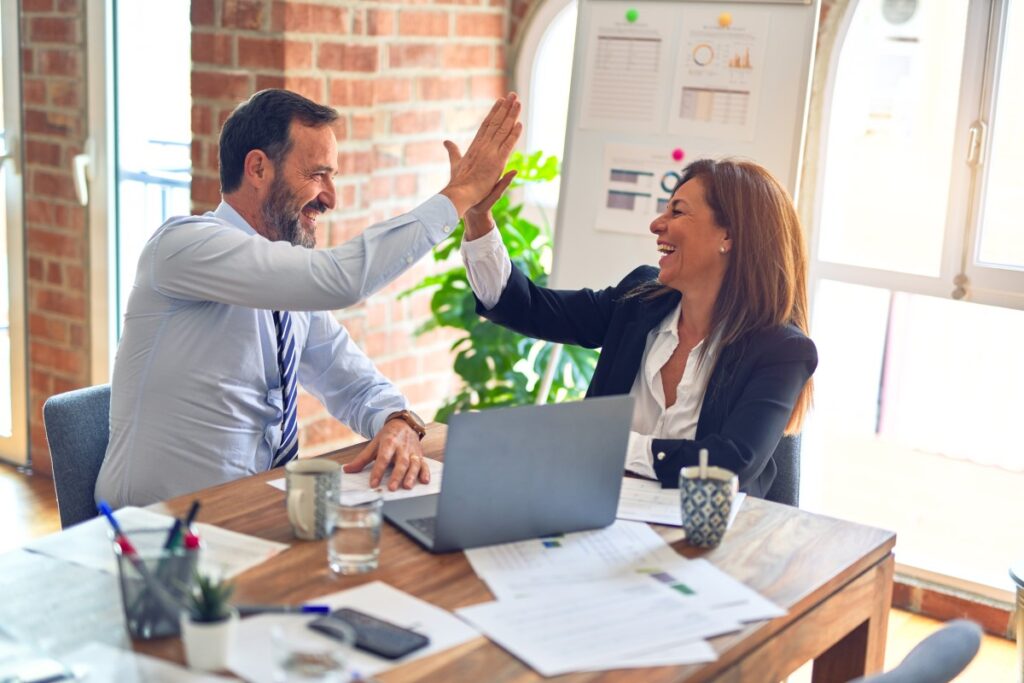 two employees smiling and hi-fiving at desk