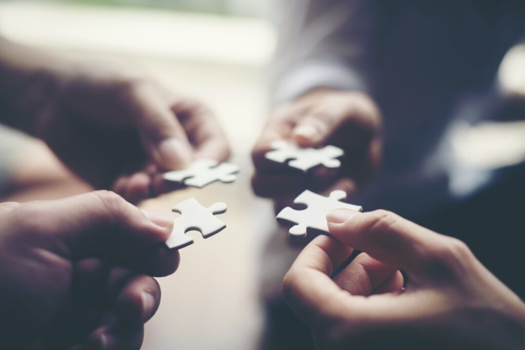 four hands holding puzzle pieces near each other